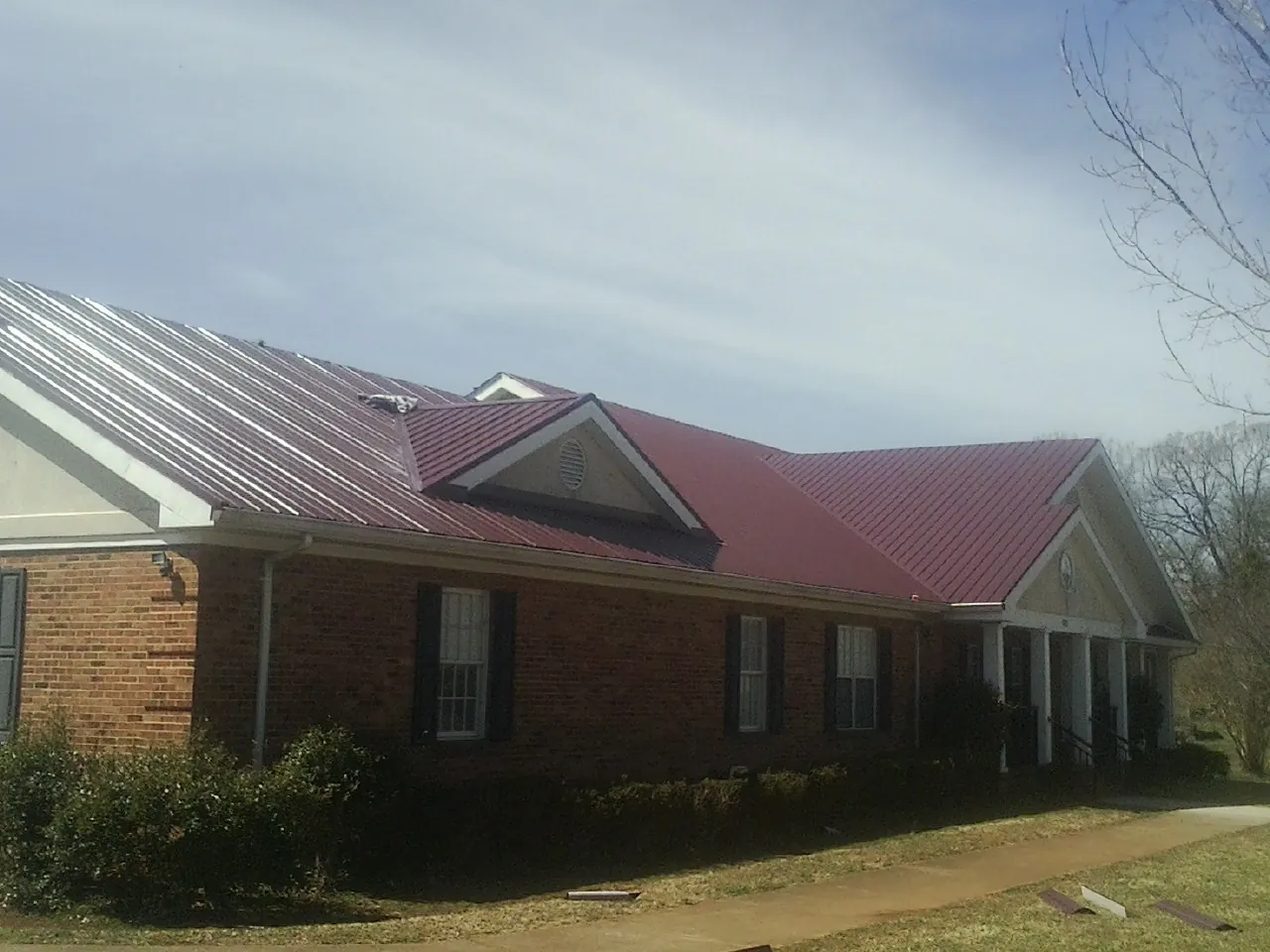 Red metal roof with gabled entries on a long brick building, from a Hail Damage Roof Repair job in Belleville